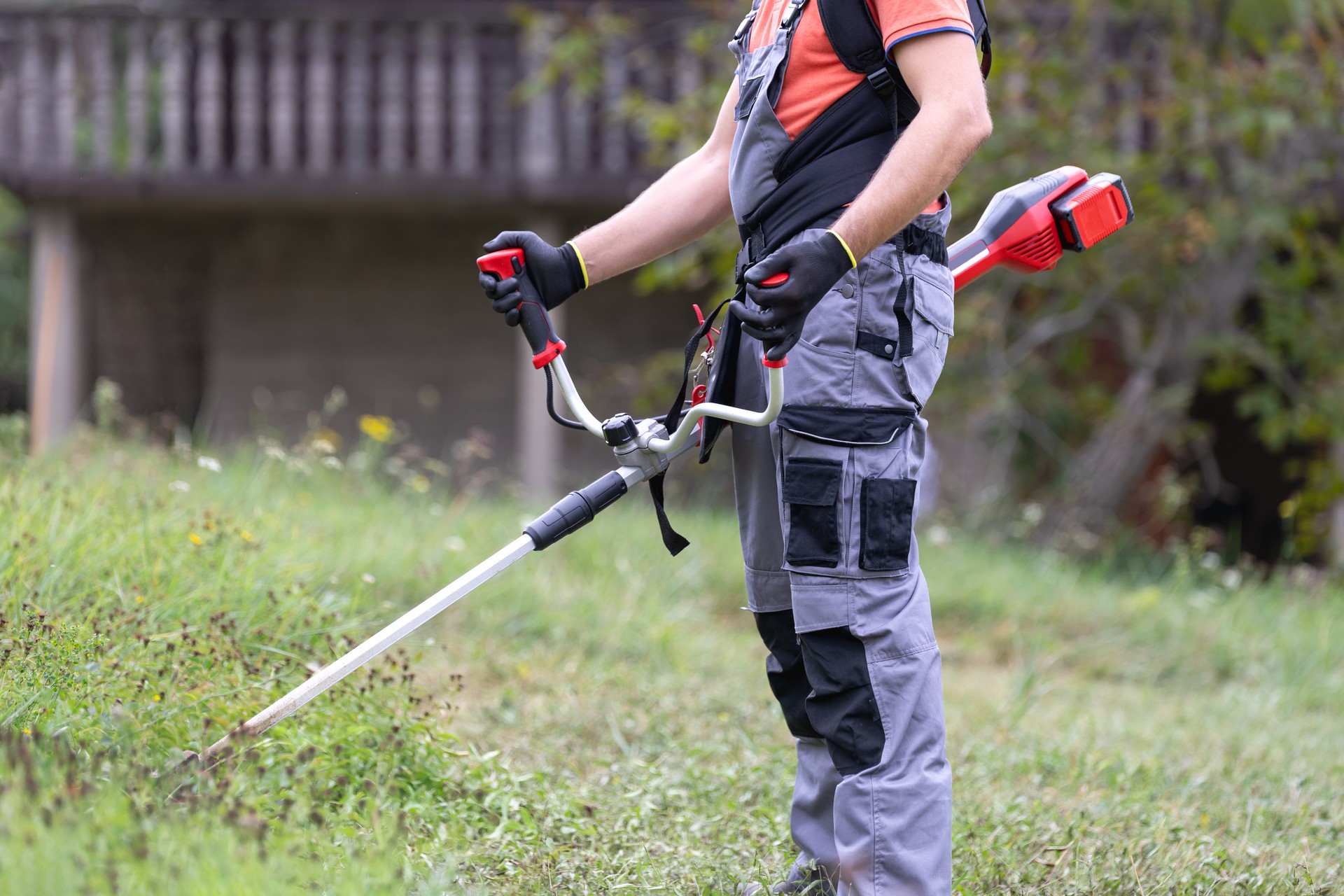 Man mowing the grass at his garden by using string trimmer with protective equipment.